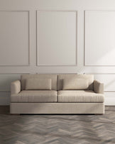 Contemporary three-seat sofa with textured beige upholstery and rectangular armrests on a herringbone-patterned wooden floor.