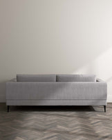 Elegant modern grey fabric sofa with a simplistic streamlined design, featuring low-profile arms, a straight backrest, and angled metal legs for a touch of contemporary chic.