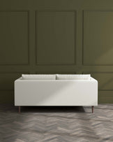 Modern minimalist white fabric sofa with cylindrical cushions and wooden tapered legs against a dark green panelled wall on a herringbone parquet floor.