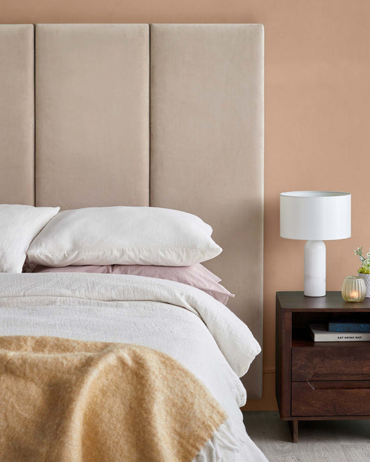 Stylish upholstered headboard, cozy bedding with layered pillows, and a modern bedside table with a lamp and decorative accents.