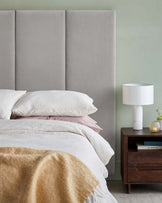 Stylish bed with plush gray headboard, layered white and pink bedding, a modern nightstand, and a sleek lamp on top.