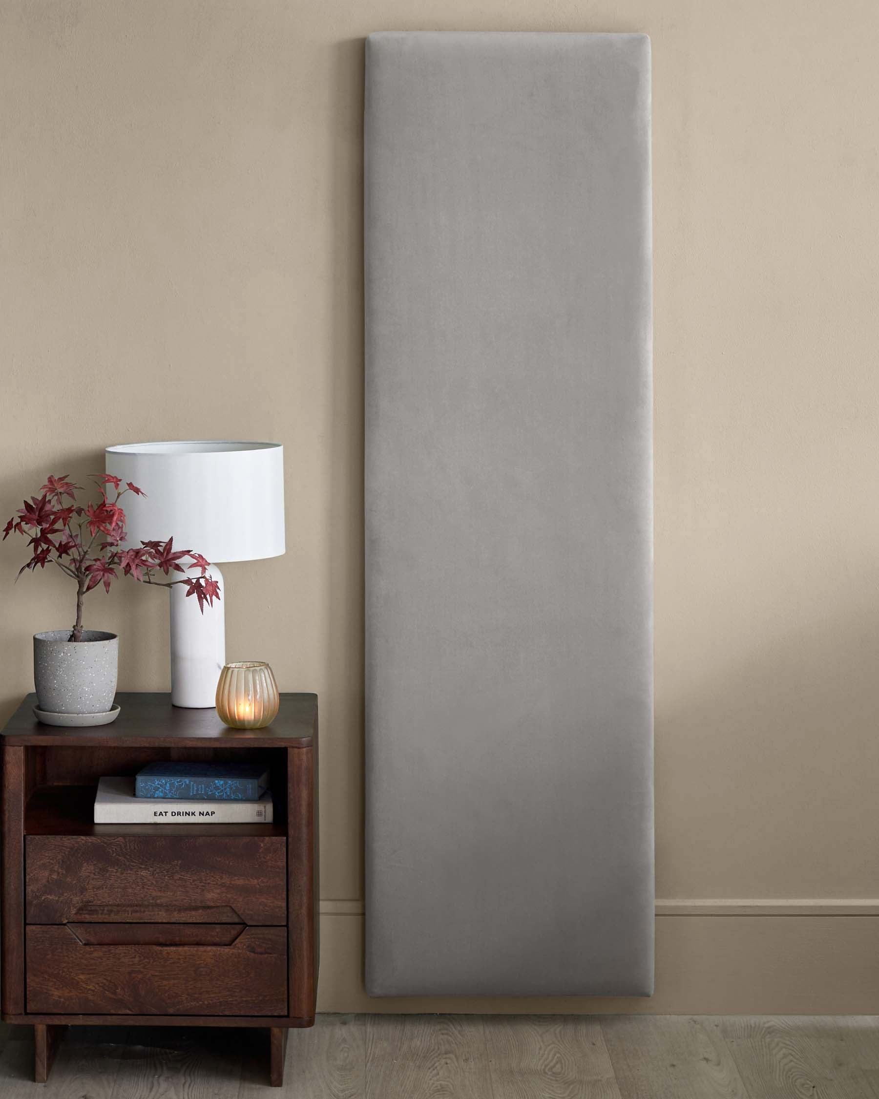 Elegant dark wood nightstand with a drawer, a white table lamp, a decorative pot, and a tall gray upholstered wall panel.