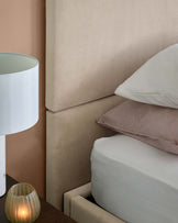 Elegant upholstered headboard with stacked pillows, a bedside lamp, and a warm candle, creating a cozy ambiance.