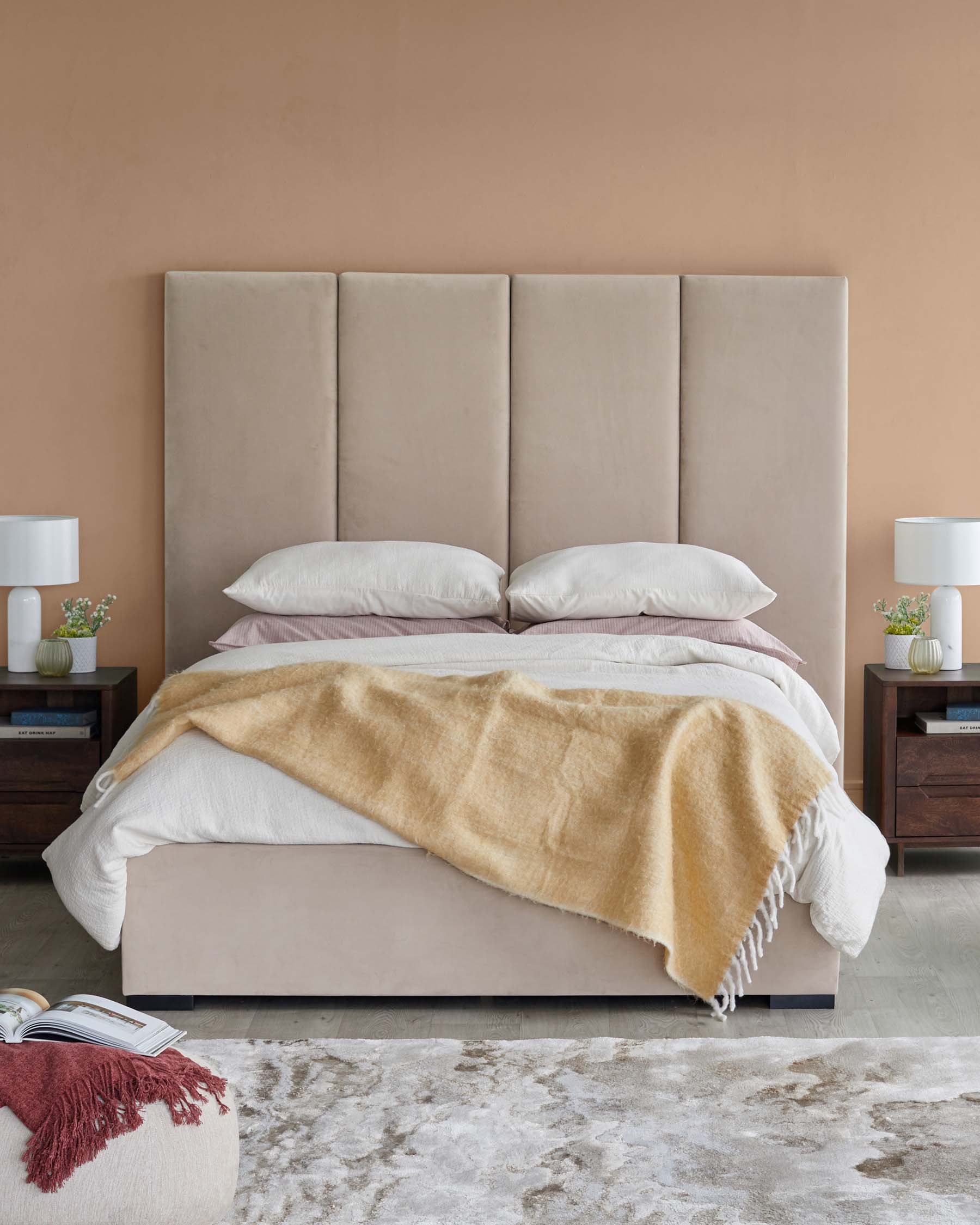 A stylish bed with a tall, soft headboard, layered bedding, nightstands with lamps, and decorative accessories on a textured rug.