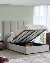 A plush, grey upholstered bed with a storage base and lift-up mattress, complemented by a modern wooden nightstand.