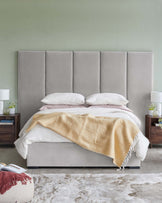 Elegant bed with a tall gray upholstered headboard, creamy linens, wooden nightstands, and decorative accessories.