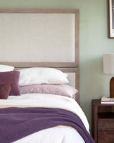 Elegant bed with a large upholstered headboard, layered pillows, a cozy blanket, and a modern side table with a lamp.