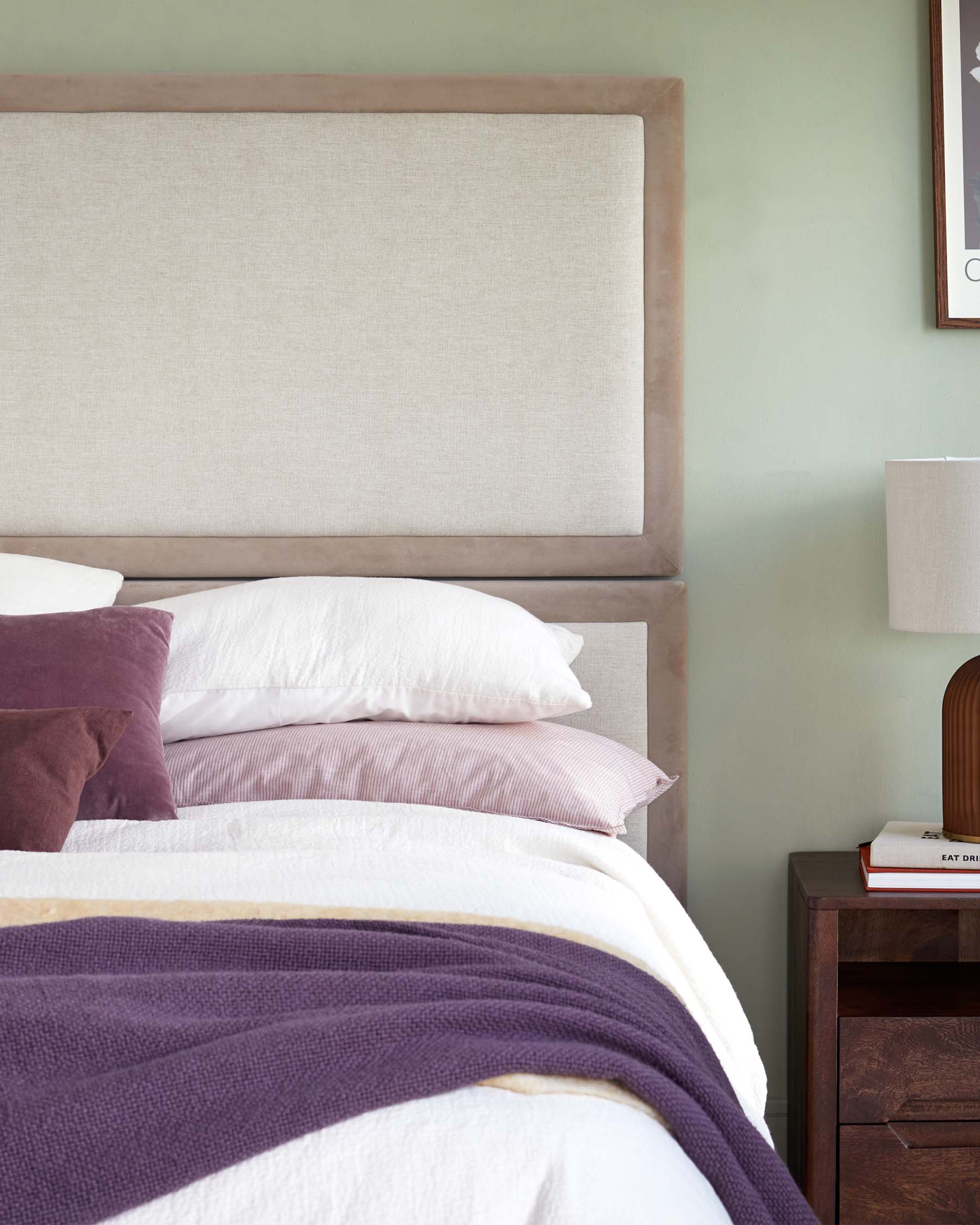 Elegant bed with a large upholstered headboard, layered pillows, a cozy blanket, and a modern side table with a lamp.