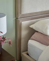 A modern upholstered bed with a textured headboard, a nightstand with a lamp, and neatly arranged pillows in soft colors.