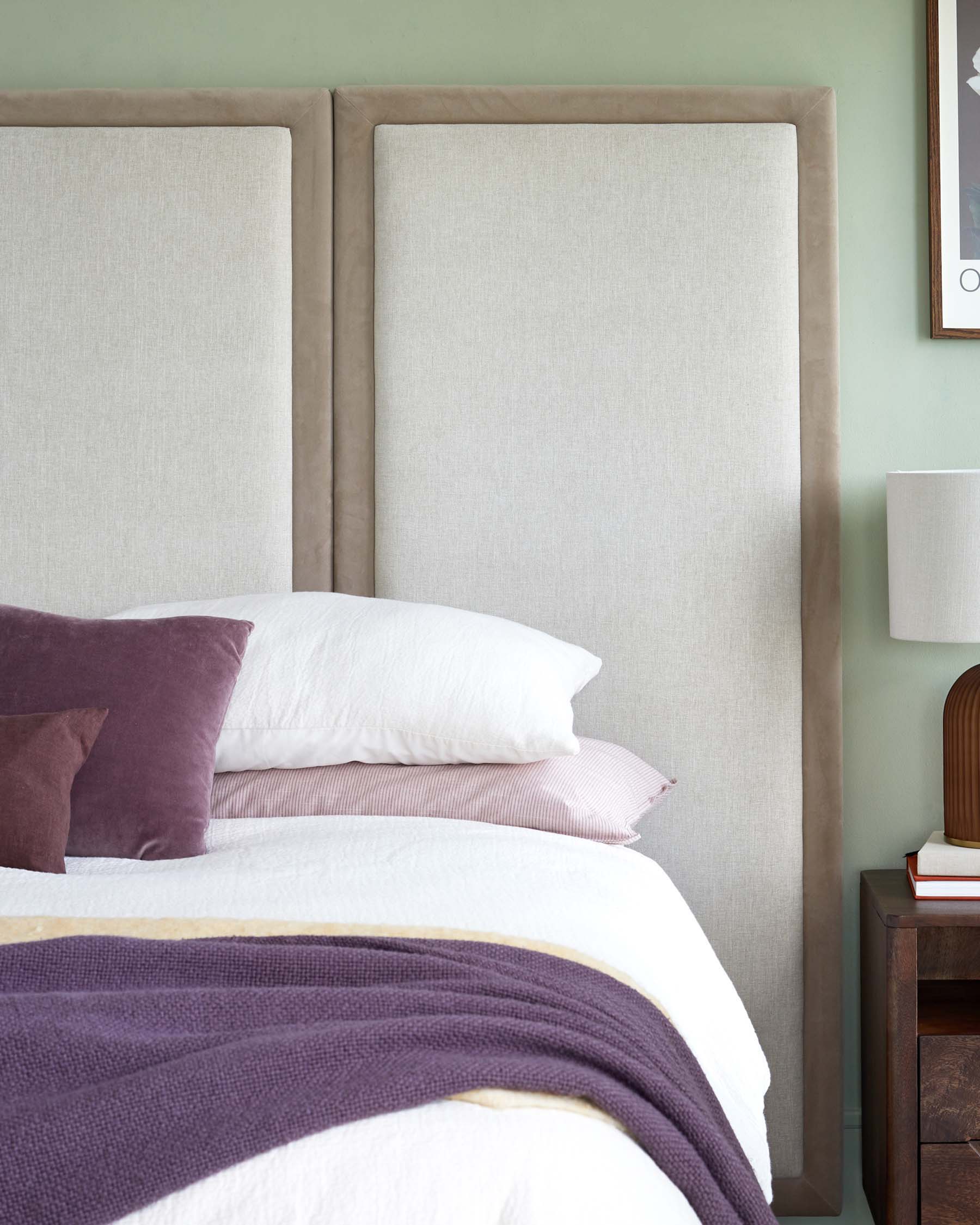 Stylish bed with padded headboard, layered pillows, a cozy throw, and a bedside table featuring a lamp and stacked books.