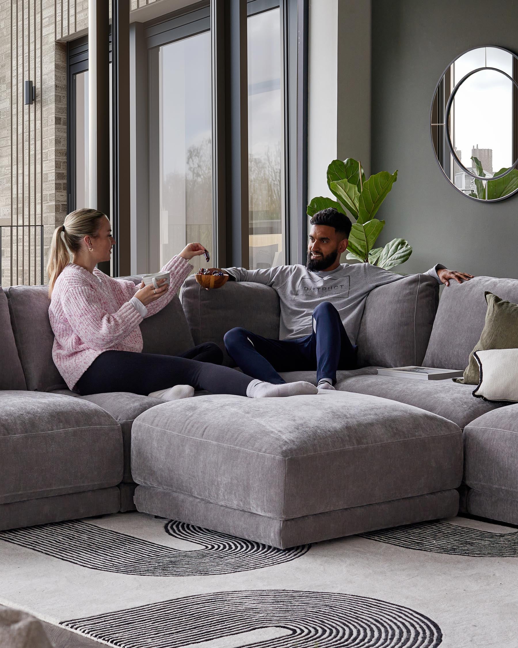 Spacious gray sectional sofa with plush seating, layered on a textured rug featuring a wavy black pattern, complemented by decorative pillows.