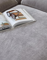 A soft gray ottoman with an open design book and stylish glasses resting on it, creating a cozy, modern aesthetic.