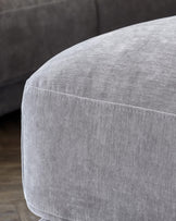 Close-up of a plush, light gray upholstered ottoman with a smooth surface and clean stitching details.