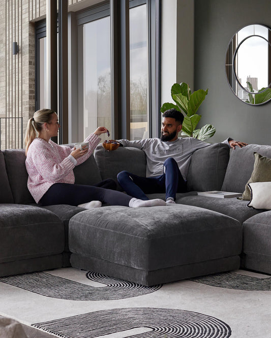 A spacious dark gray sectional sofa with soft cushions, paired with a stylish area rug featuring a curved black design.