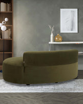 A curved, olive green sofa with soft upholstery, complemented by a minimalist side table and decorative items in a stylish setting.