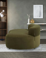 Curved olive green sofa paired with a decorative side table and modern floor lamp, set against a stylish backdrop.