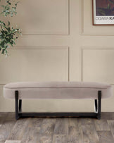 Sleek, modern bench in soft beige upholstery, supported by a stylish black frame, set against a neutral wall backdrop.