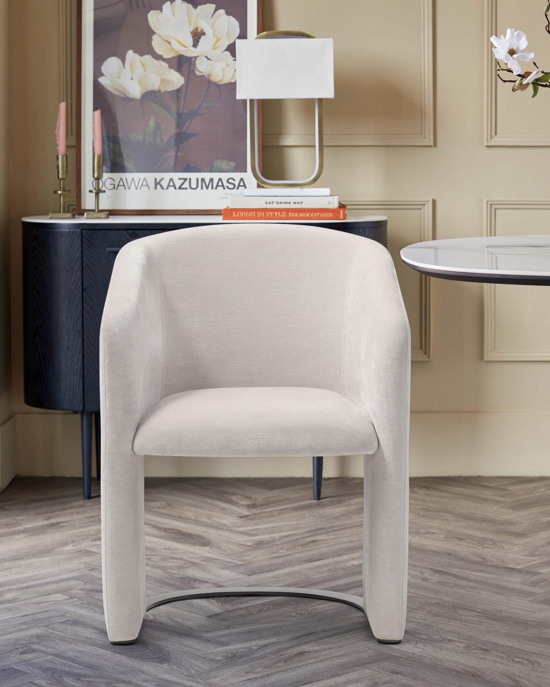 A sleek, cream-colored armchair with soft curves and a modern design, complemented by a stylish table and decor in a chic setting.