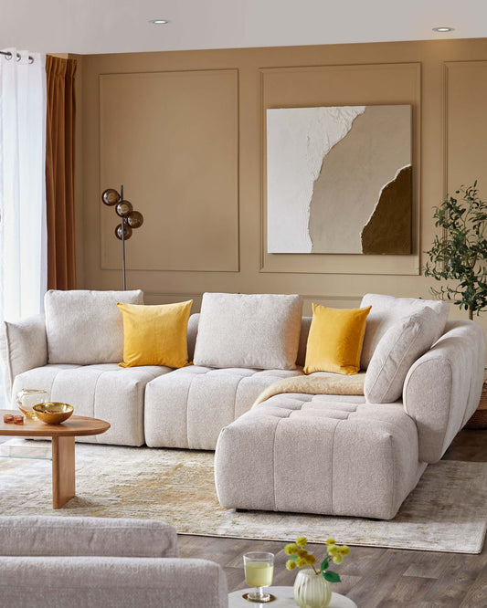 Modern beige sectional sofa with yellow accent pillows, paired with a round wooden coffee table, set against a neutral backdrop.