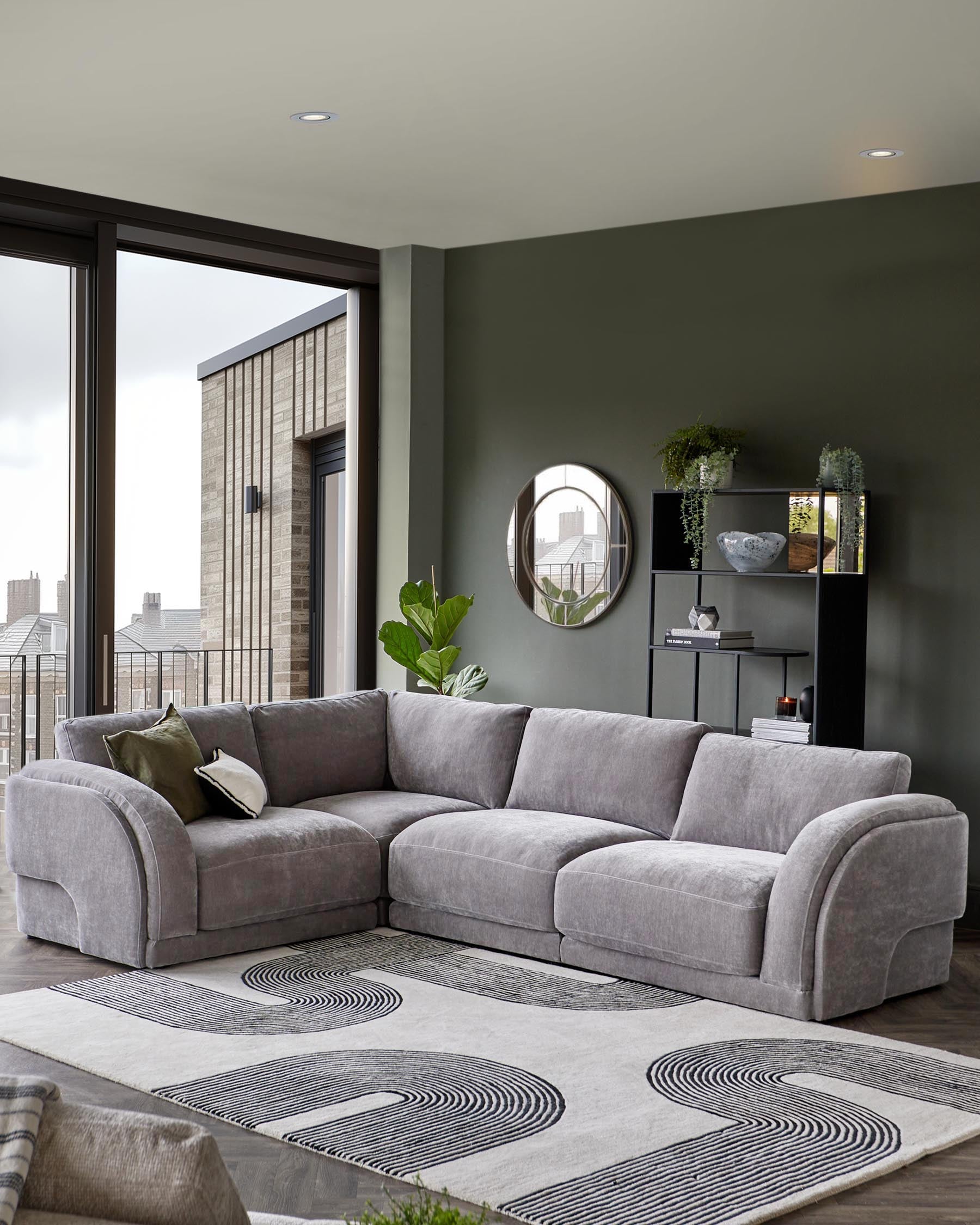 A plush gray sectional sofa, a geometric area rug, a sleek black shelf with decor, and a round wall mirror.