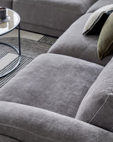 A plush gray sectional sofa with soft cushions and decorative pillows, complemented by a sleek round glass coffee table.