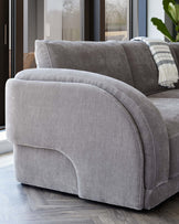 Curved, plush gray sofa showcasing a soft fabric finish, designed for comfort and modern aesthetics. Perfect for cozy living spaces.