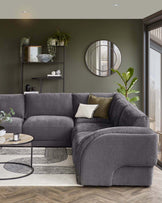 Stylish grey sectional sofa with soft cushions, round coffee table, patterned rug, and modern shelving with greenery.