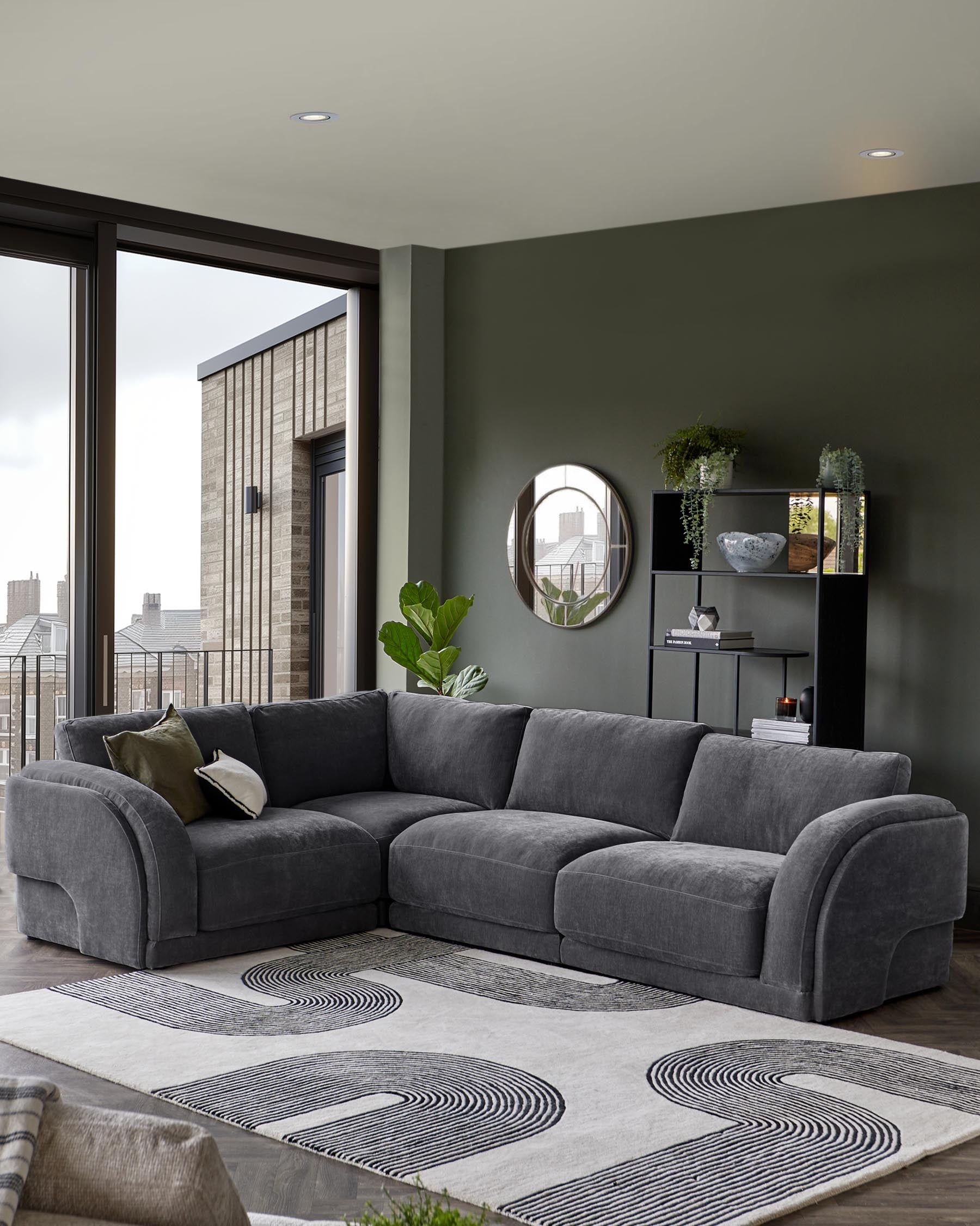 A cozy gray sectional sofa, geometric rug, modern black shelving unit, and a round mirror adorn a stylish living space.