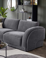 A plush gray sectional sofa with rounded edges, complemented by a glass coffee table and stylish shelving unit in a chic setting.