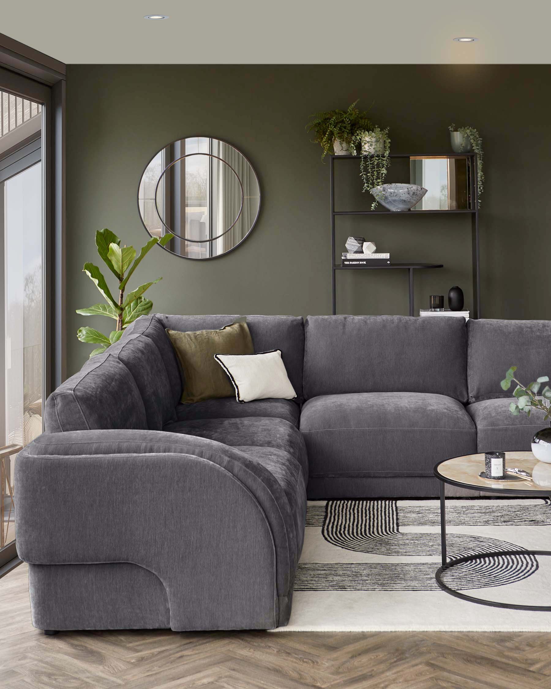 Modern grey sectional sofa with a decorative pillow, round coffee table, and a stylish shelf with plants and decor against a green wall.