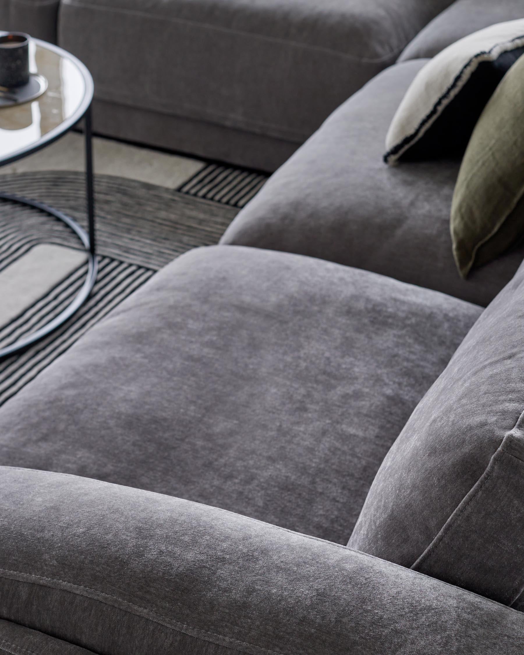 Stylish grey velvet sectional sofa with plush cushions, paired with a sleek glass-top coffee table and a patterned area rug.