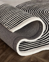 Black and white striped area rug with a modern design, rolled halfway to reveal a textured underside, on a wooden floor.