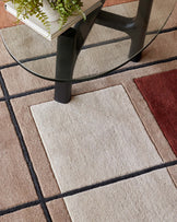 Modern round glass-top coffee table with a sleek black metal frame, perched on a contemporary geometric patterned area rug in a warm neutral palette.