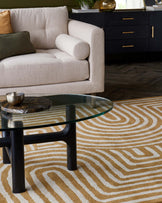 Elegant modern living room furniture featuring a beige fabric sofa with a clean, minimalist design, a cylindrical bolster pillow, and plush cushioning. In the foreground, a contemporary round glass coffee table with a unique black base adds a touch of sophistication. In the background, a sleek black sideboard with gold handles contributes to the room's upscale ambiance. The scene is grounded by a textured cream and gold wave-patterned area rug.