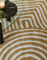 A contemporary round glass-top coffee table with a black marble base, perched on a geometric patterned rug in shades of tan and cream.