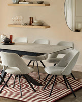 Modern dining room furniture consisting of a rectangular black dining table with sleek lines, and six upholstered dining chairs in light grey fabric with dark angled legs. The setup is complemented by a patterned red and cream area rug and two wooden floating shelves mounted on the wall above, displaying dinnerware and decorative objects. A round edge mirror partially reflects the room, amplifying the space.