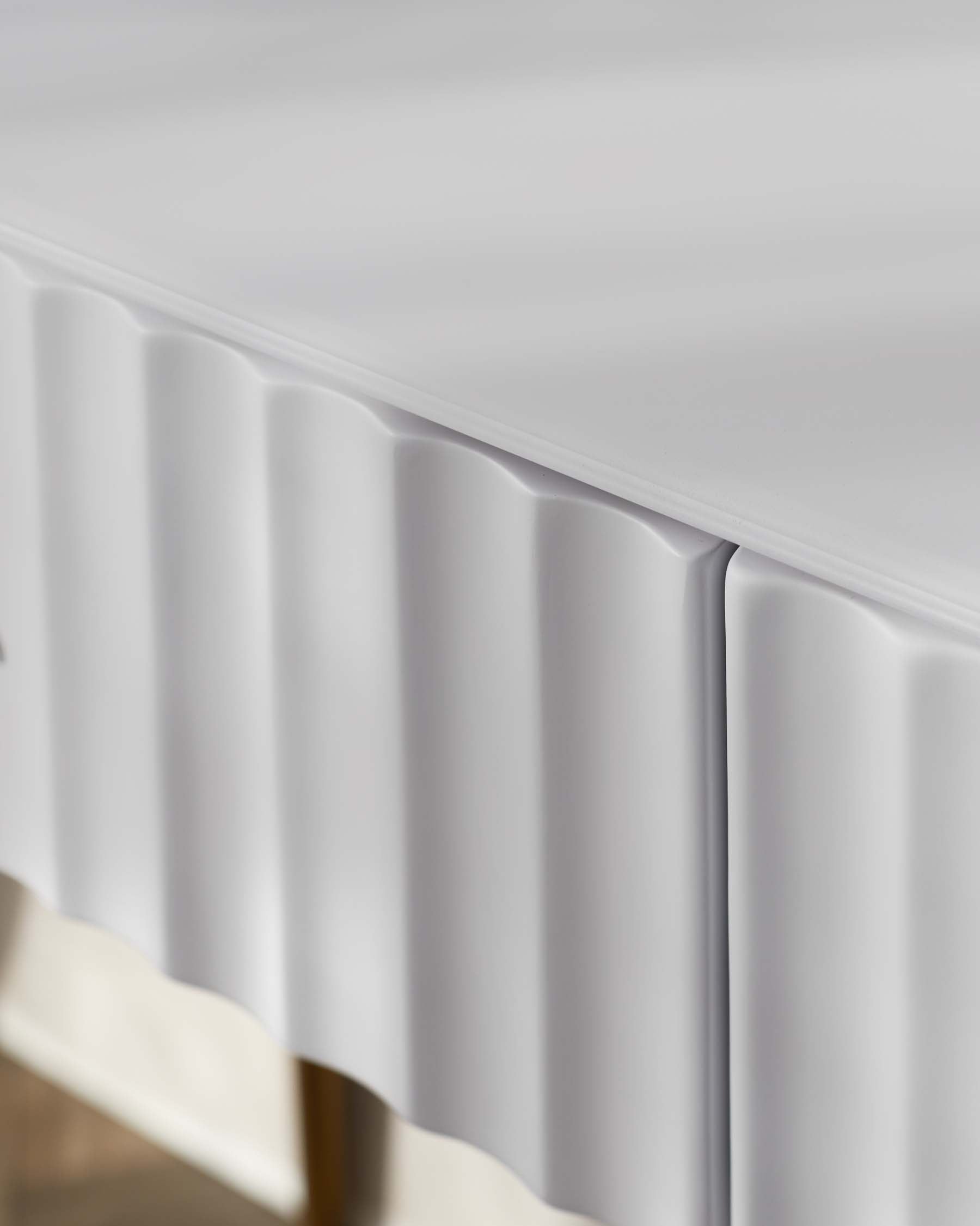 Close-up of a modern white cabinet with a smooth top surface and a vertically fluted front face, featuring a contemporary design with clean lines and minimalistic appeal.