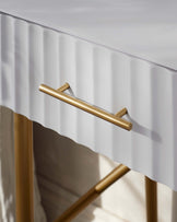 Close-up of a modern white drawer front with a sleek, gold metal handle, and a glimpse of a matching gold-framed structure, possibly part of a chic, contemporary furniture piece.