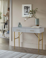 Stylish console table with a grey top, gold legs, two drawers, and decorative accents like a vase and stacked books.