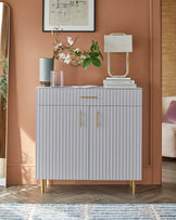 Contemporary gray cabinet with vertical grooves, gold handles, a modern lamp, and decorative vases on a warm-toned wall.