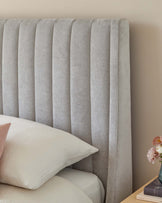 Vertical channel-tufted headboard in a light grey fabric, accompanied by neutral toned bedding and a bedside nightstand with floral decoration.