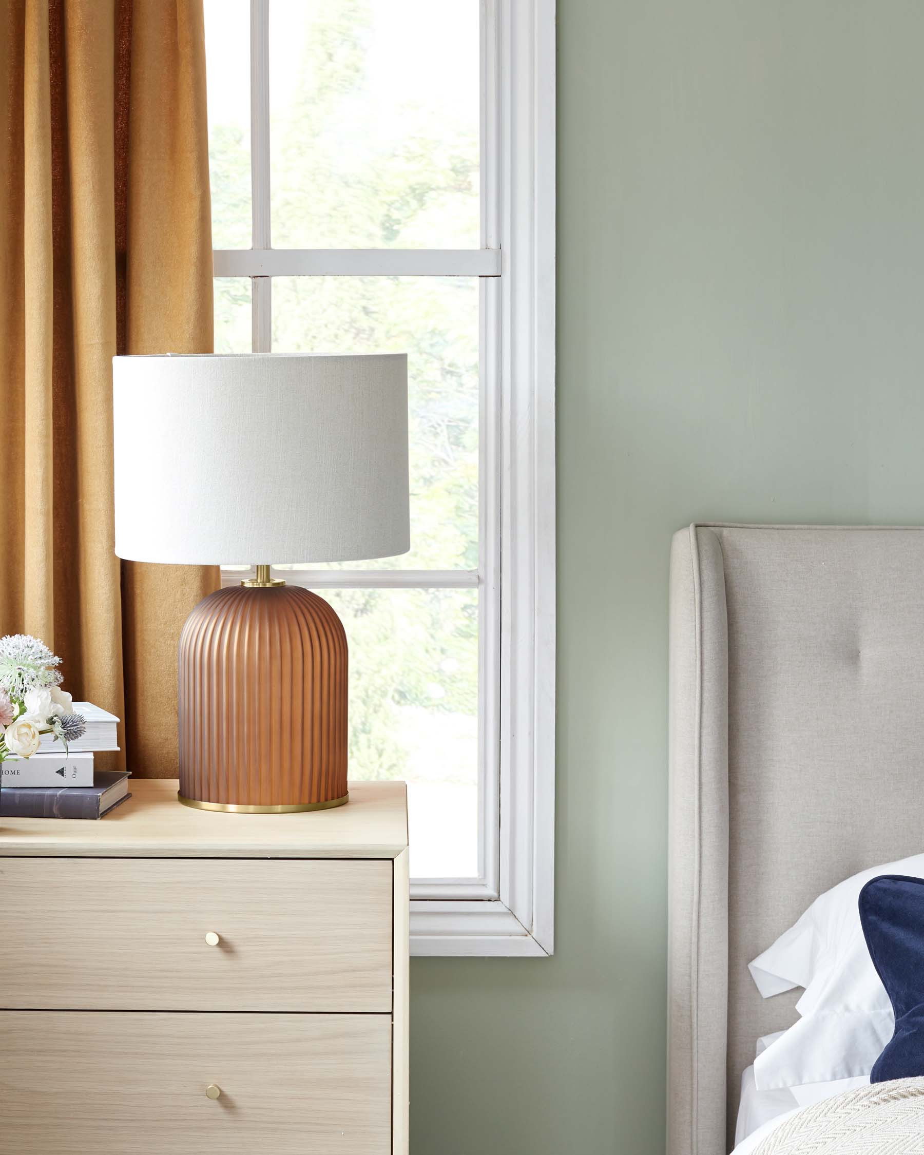 Modern natural wood bedside table with open shelf and two drawers, featuring round brass handles next to an upholstered bed with neutral-tone headboard.