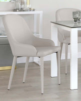 A sleek beige chair with curved contours, paired with a glass-top table and minimalist white legs, enhancing a modern dining space.