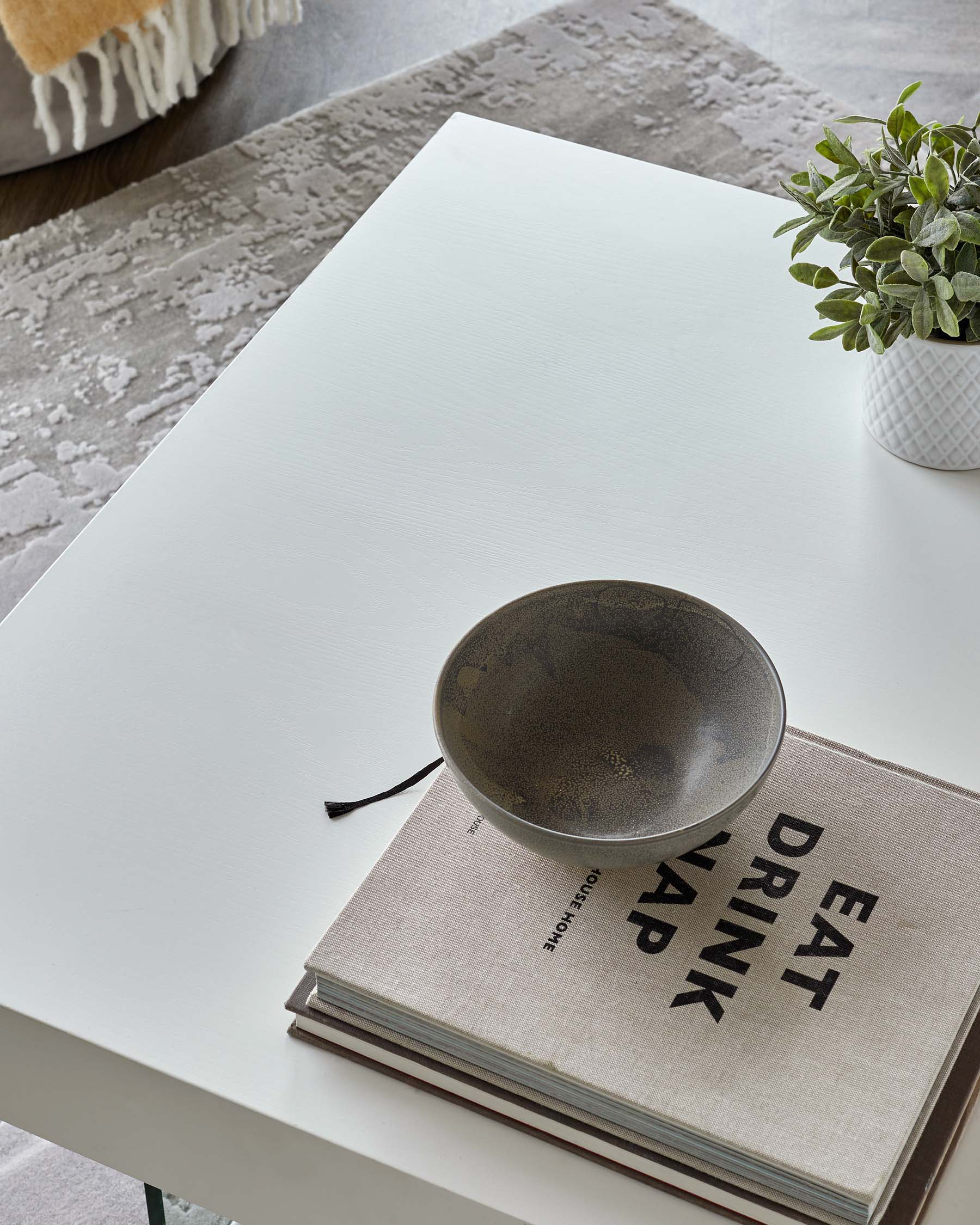 A modern white coffee table topped with a decorative bowl and stacked books, complemented by a small potted plant.