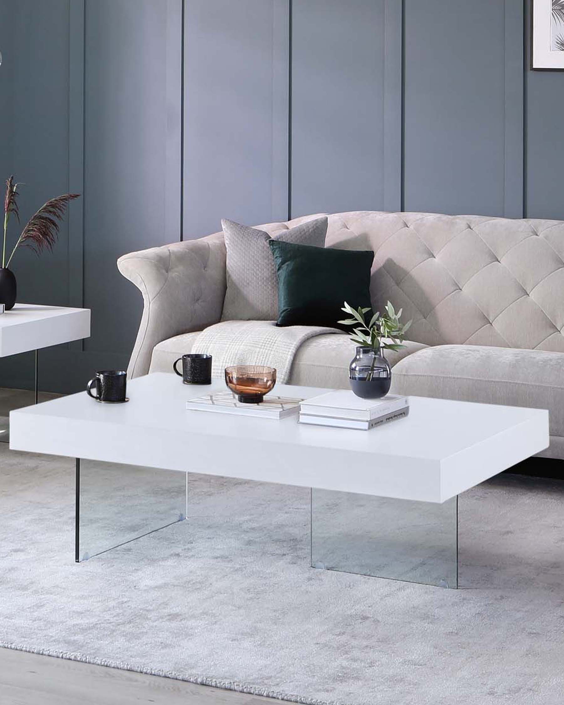 A tufted gray sofa with decorative pillows, paired with a sleek white coffee table on transparent legs, and stylish decor items.