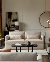 Elegant living room interior featuring a plush, light taupe three-seat sofa with soft fabric upholstery and matching side armrests. In front of the sofa is an oval-shaped, black coffee table with a sleek design. A smaller side table with a dark surface and thin legs is to the side, supporting a lamp with a unique ribbed base and a white shade. Completing the scene is a beige accent armchair with a modern silhouette to the right, harmonizing with the room's warm neutral tones and sophisticated ambiance.