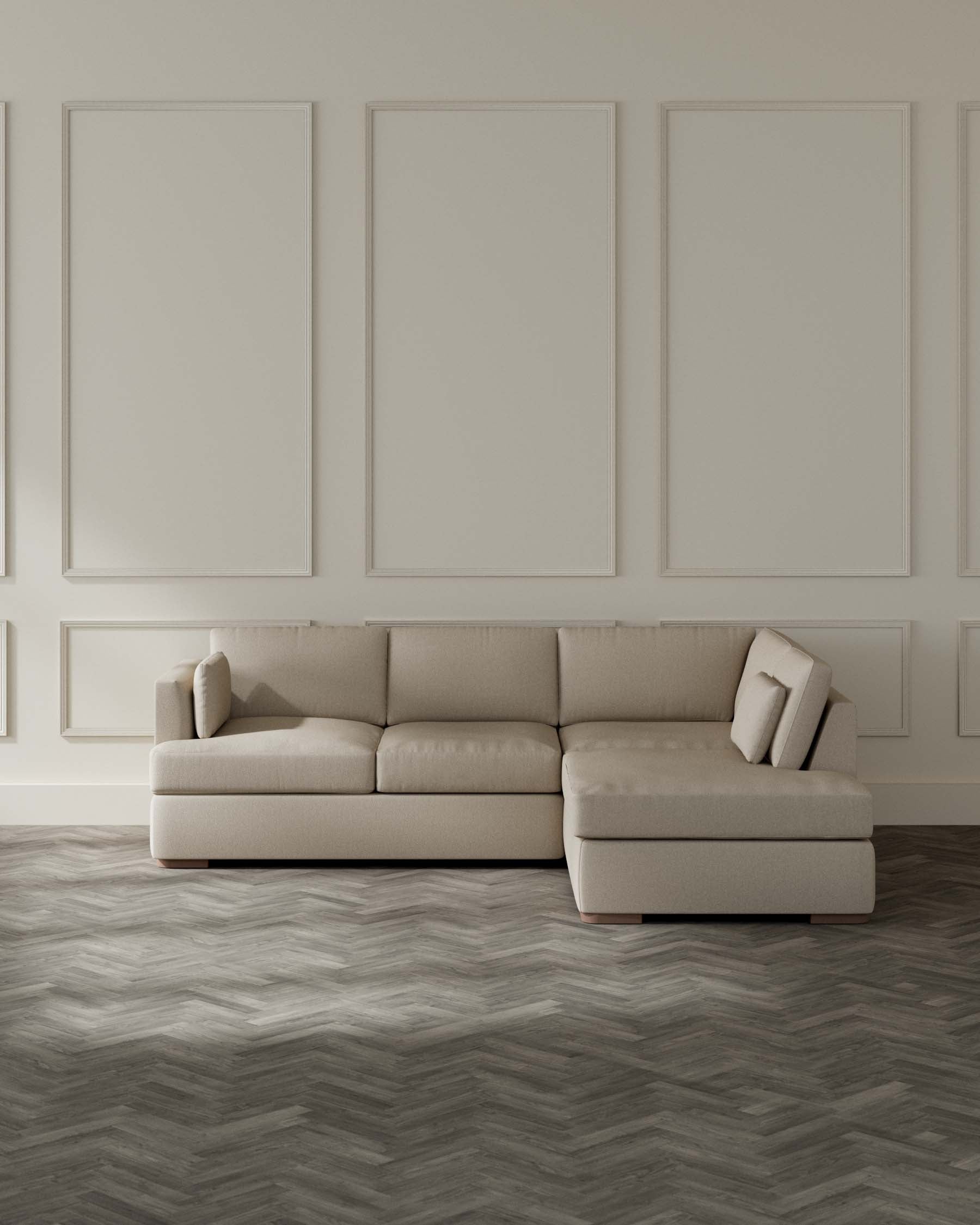 A contemporary beige sectional sofa with a chaise on one end, featuring a minimalist design and clean lines, cushions included, set against a neutral wall with decorative panelling, atop a herringbone patterned wood floor.