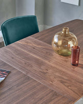 A modern rectangular wooden dining table with a visible wood grain pattern accompanied by a green velvet upholstered dining chair with a curved backrest, set in a room with a neutral colour palette.