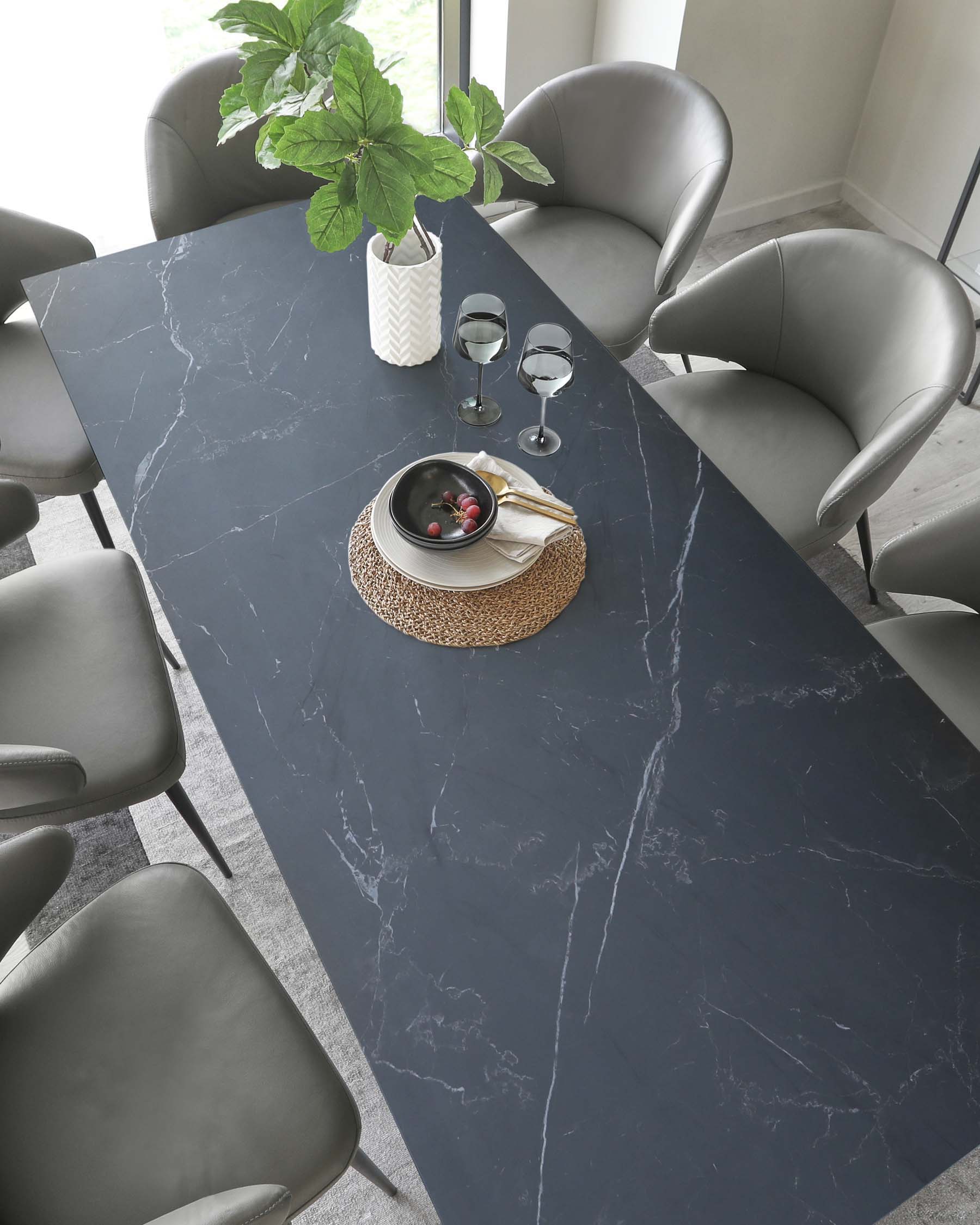 Elegant dining room set featuring a large rectangular marble table with a dark surface and distinctive white veining. The table is surrounded by sleek grey upholstered chairs with a modern design that includes curved backs for comfort. The overall aesthetic is contemporary with a luxurious feel.