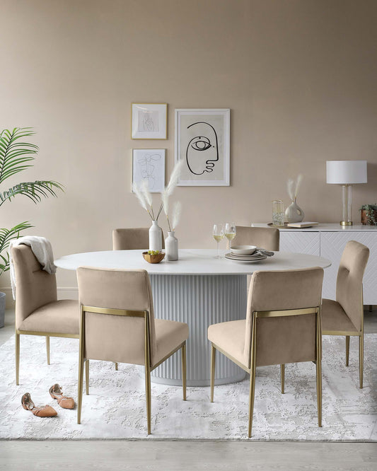 A circular dining table with a fluted base surrounded by four beige upholstered chairs with gold legs, set on a decorative rug.